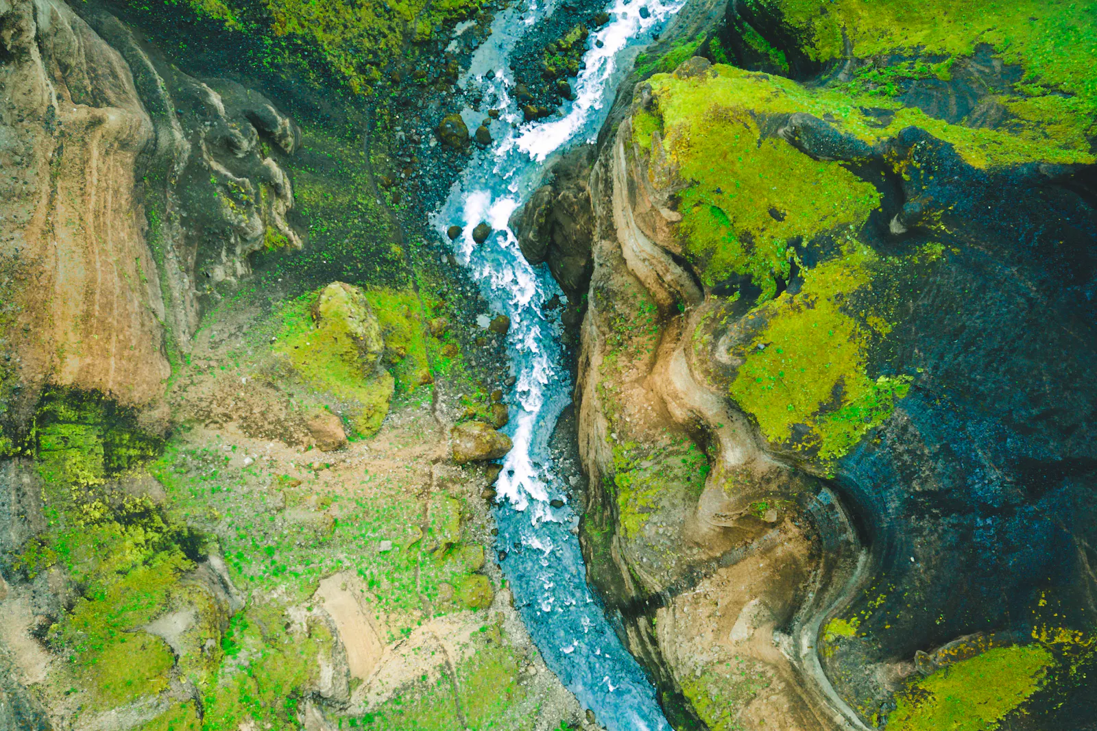 A turquoise river winding through a steep, moss-covered gorge.