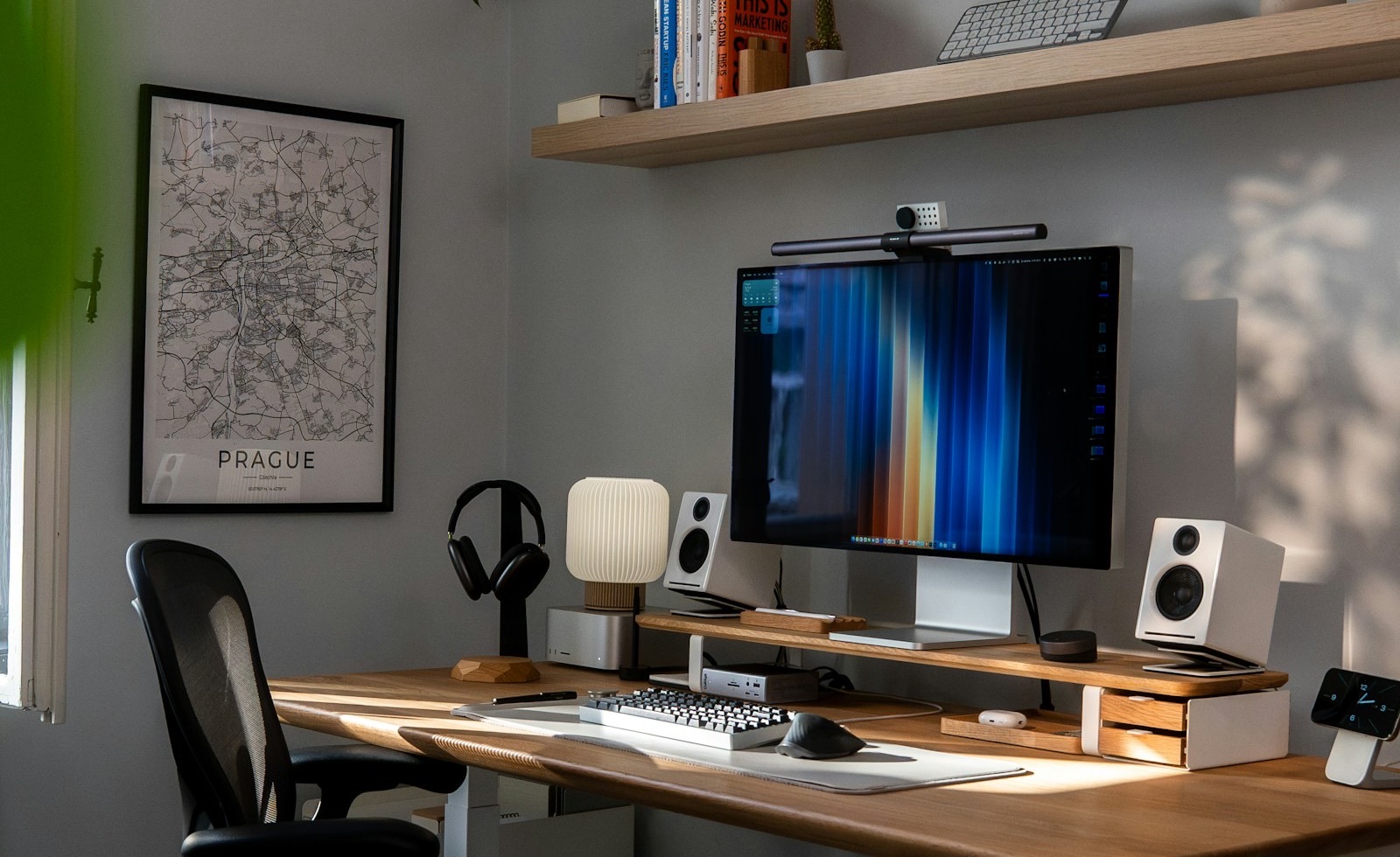 A home office: a monitor on a wooden desk under shelves of books and plants, in daylight